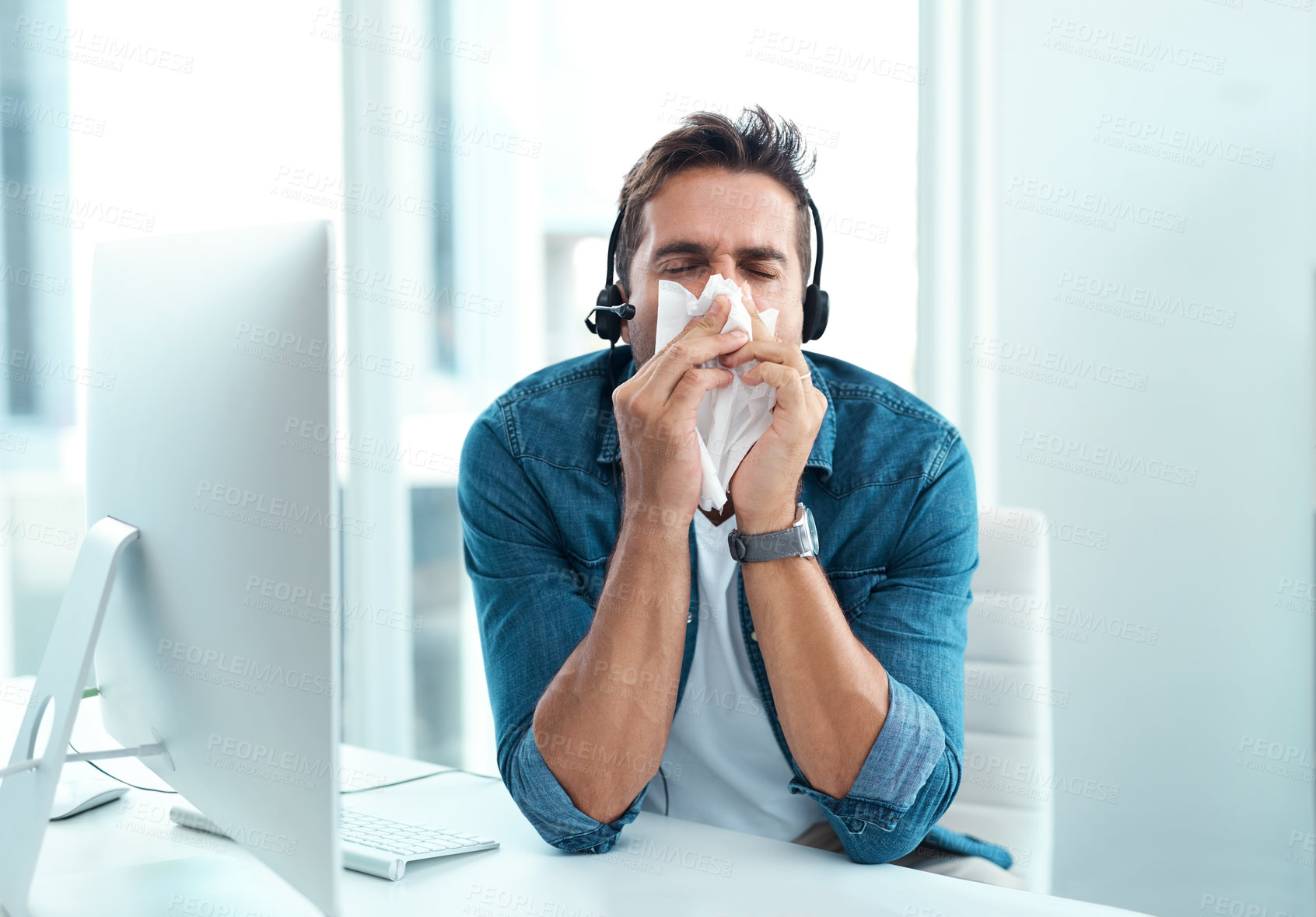 Buy stock photo Shot of a male call centre agent blowing his nose with a tissue in his office