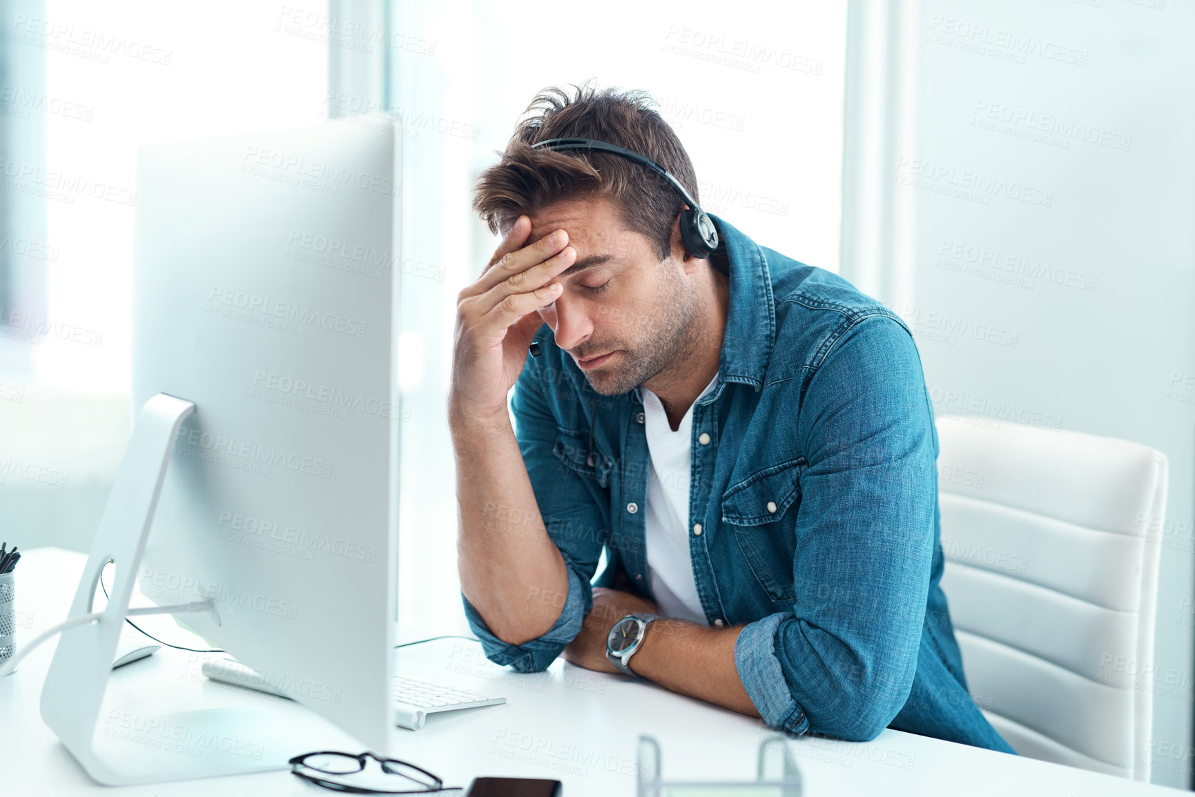 Buy stock photo Shot of a young male call centre agent suffering from a headache in his office