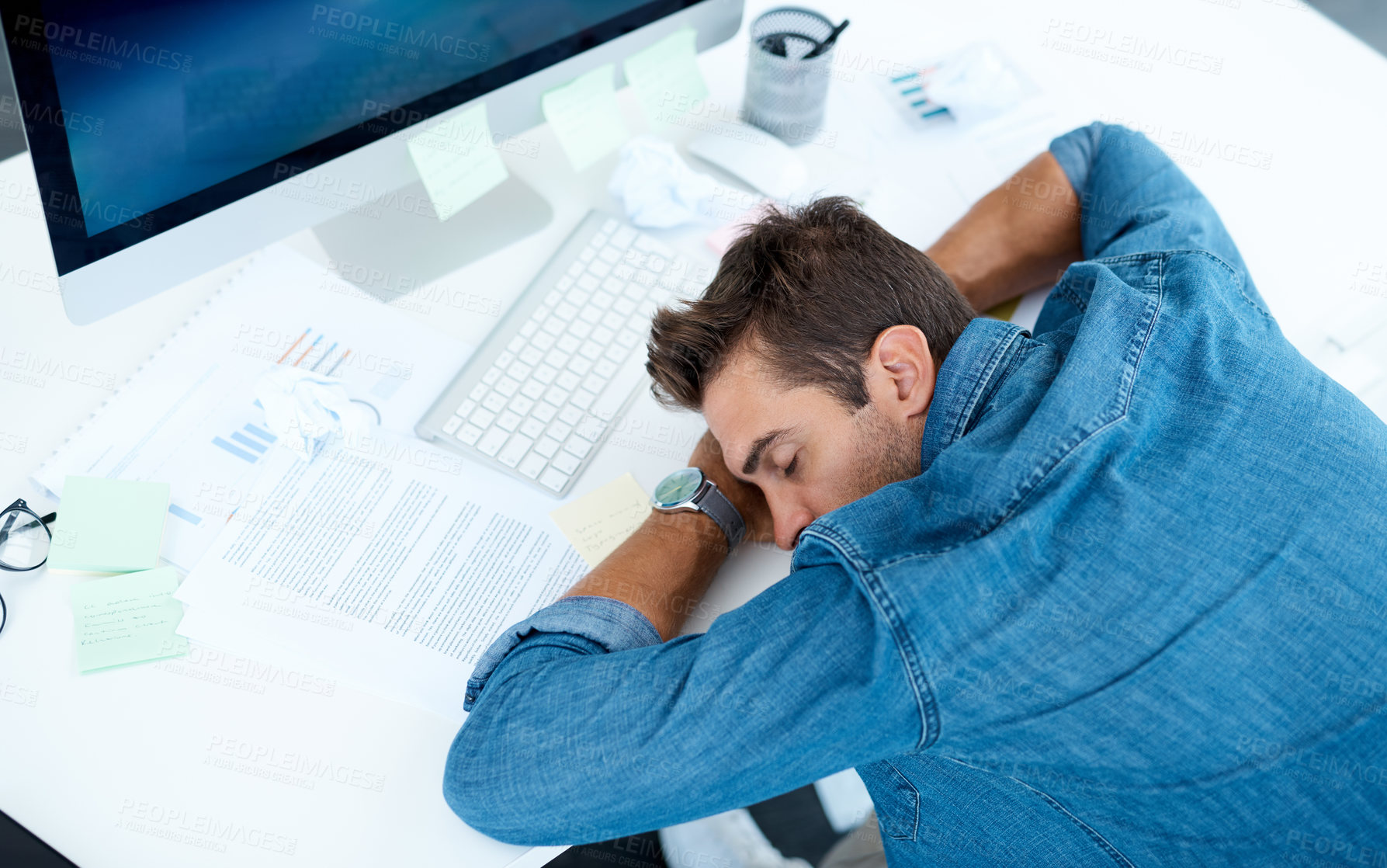 Buy stock photo High angle shot of an exhausted young businessman taking a nap on his desk in his office