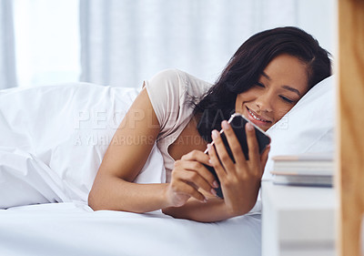 Buy stock photo Shot of a young woman waking up in the morning and using her phone in bed