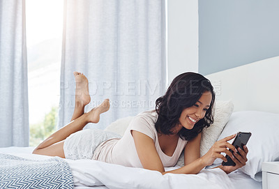 Buy stock photo Shot of a young woman waking up in the morning and using her phone in bed