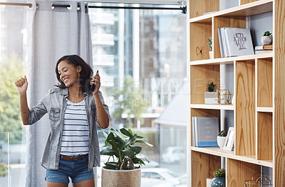 Buy stock photo Shot of a young woman dancing while listening to music from her cellphone at home