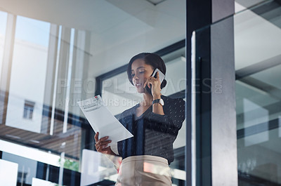 Buy stock photo Shot of a young businesswoman talking on a cellphone while going through paperwork in an office