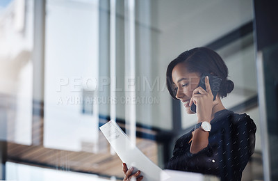 Buy stock photo Shot of an attractive young businesswoman using a smartphone and reading a document in a modern office