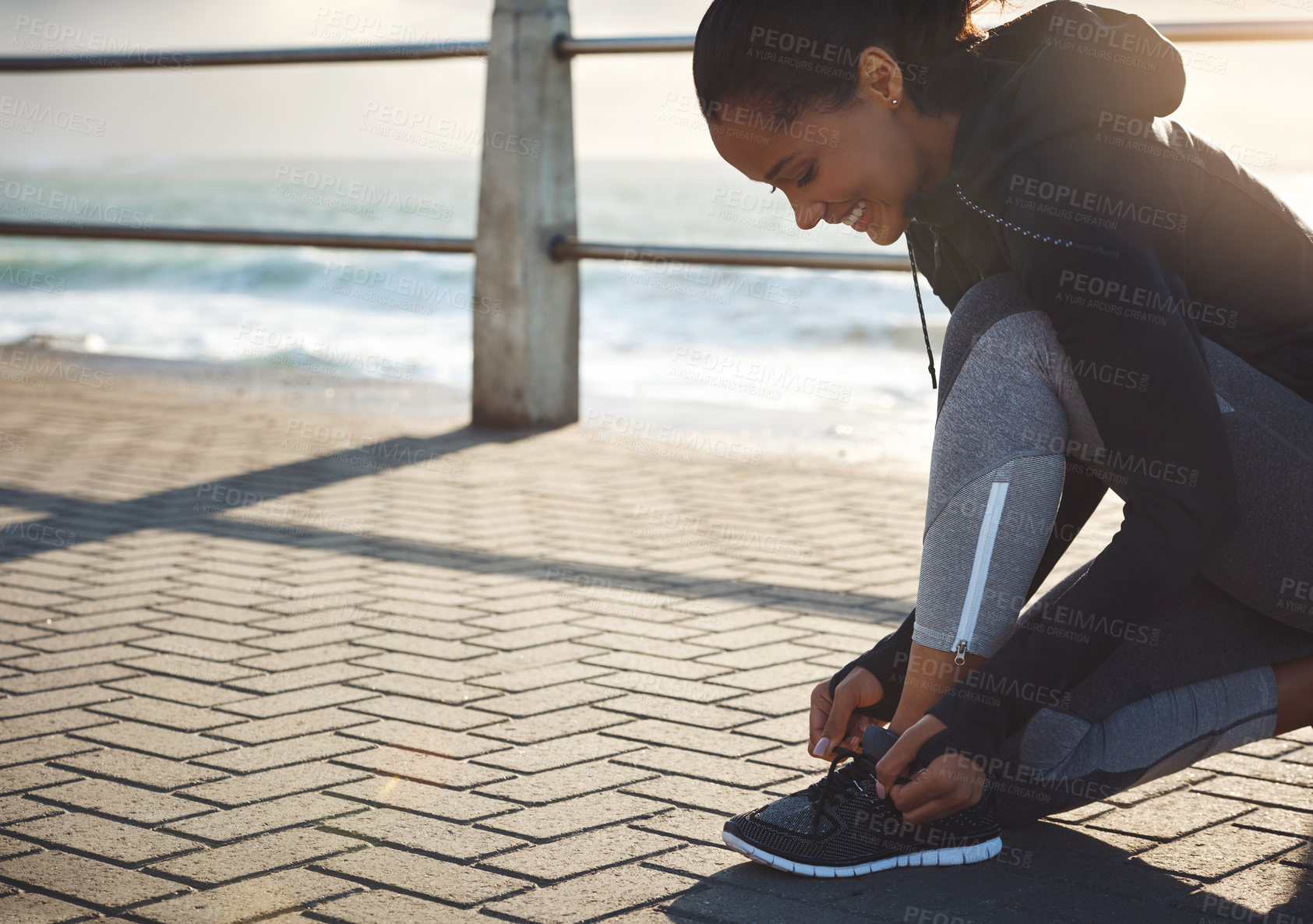 Buy stock photo Shot of a fit young woman tying her shoelaces before going for a run on the promenade