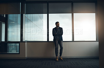 Buy stock photo Shot of a young businessman leaning against a wall and looking thoughtful in a modern office
