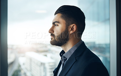 Buy stock photo Shot of a young businessman looking thoughtfully out of an office window