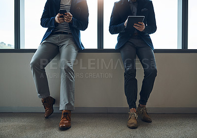 Buy stock photo Cropped shot of two businessmen using a digital tablet and cellphone while leaning against a wall in a modern office