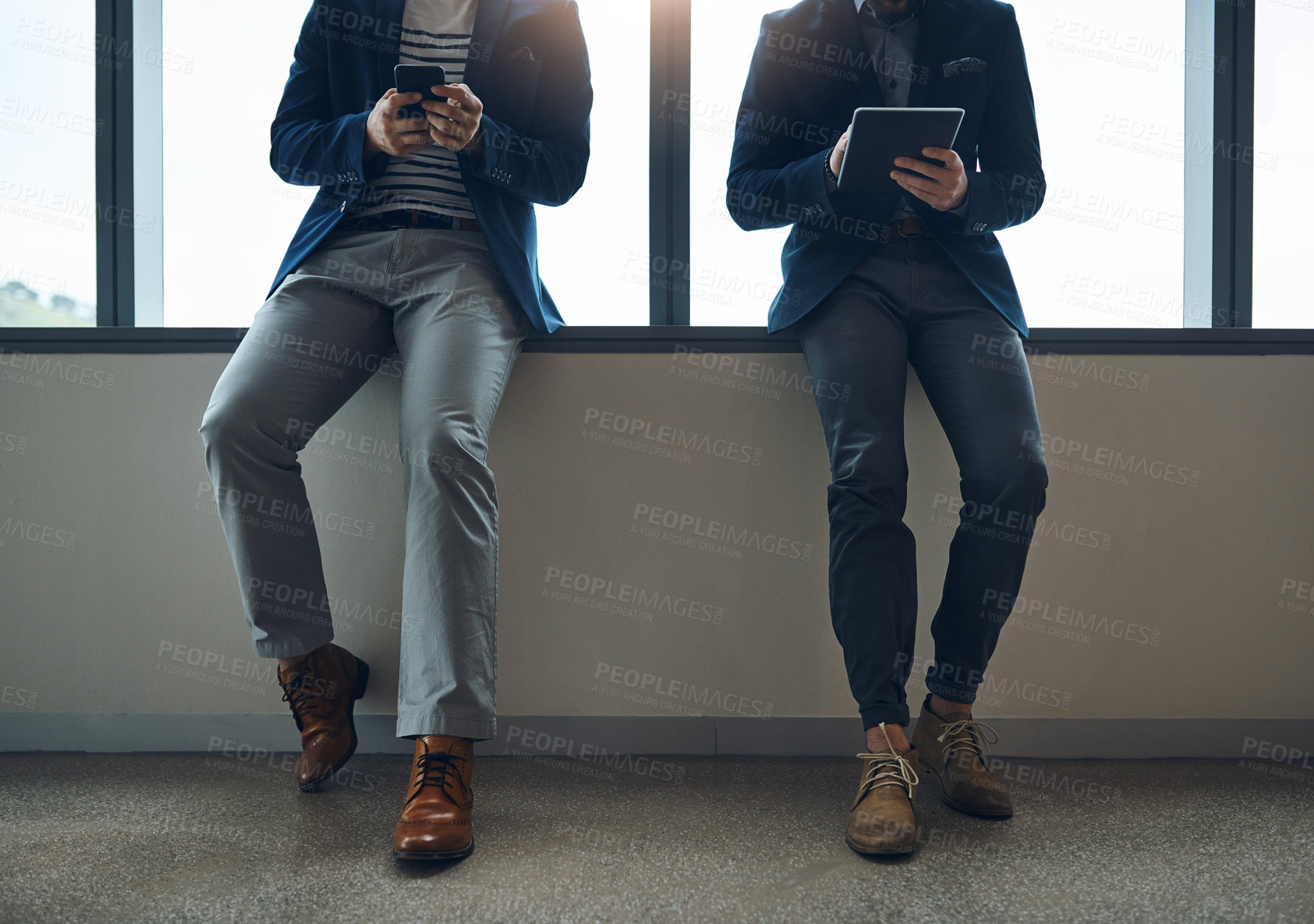 Buy stock photo Cropped shot of two businessmen using a digital tablet and cellphone while leaning against a wall in a modern office