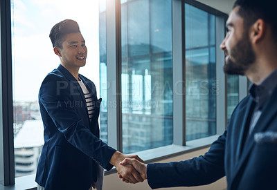 Buy stock photo Shot of two young businessmen shaking hands in a modern office