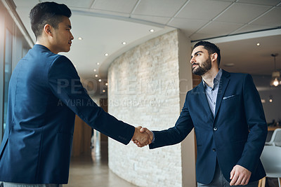 Buy stock photo Shot of two young businessmen shaking hands in a modern office
