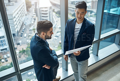 Buy stock photo Shot of two young businessmen discussing paperwork in a modern office