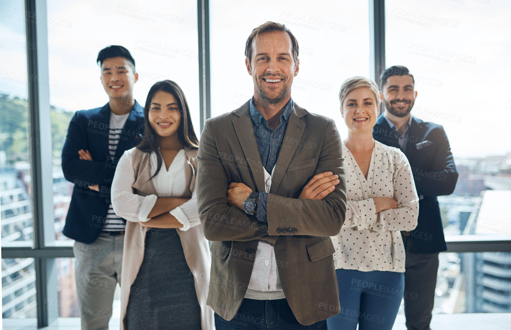 Buy stock photo Portrait of a group of confident young businesspeople standing together with their arms folded inside the office during the day
