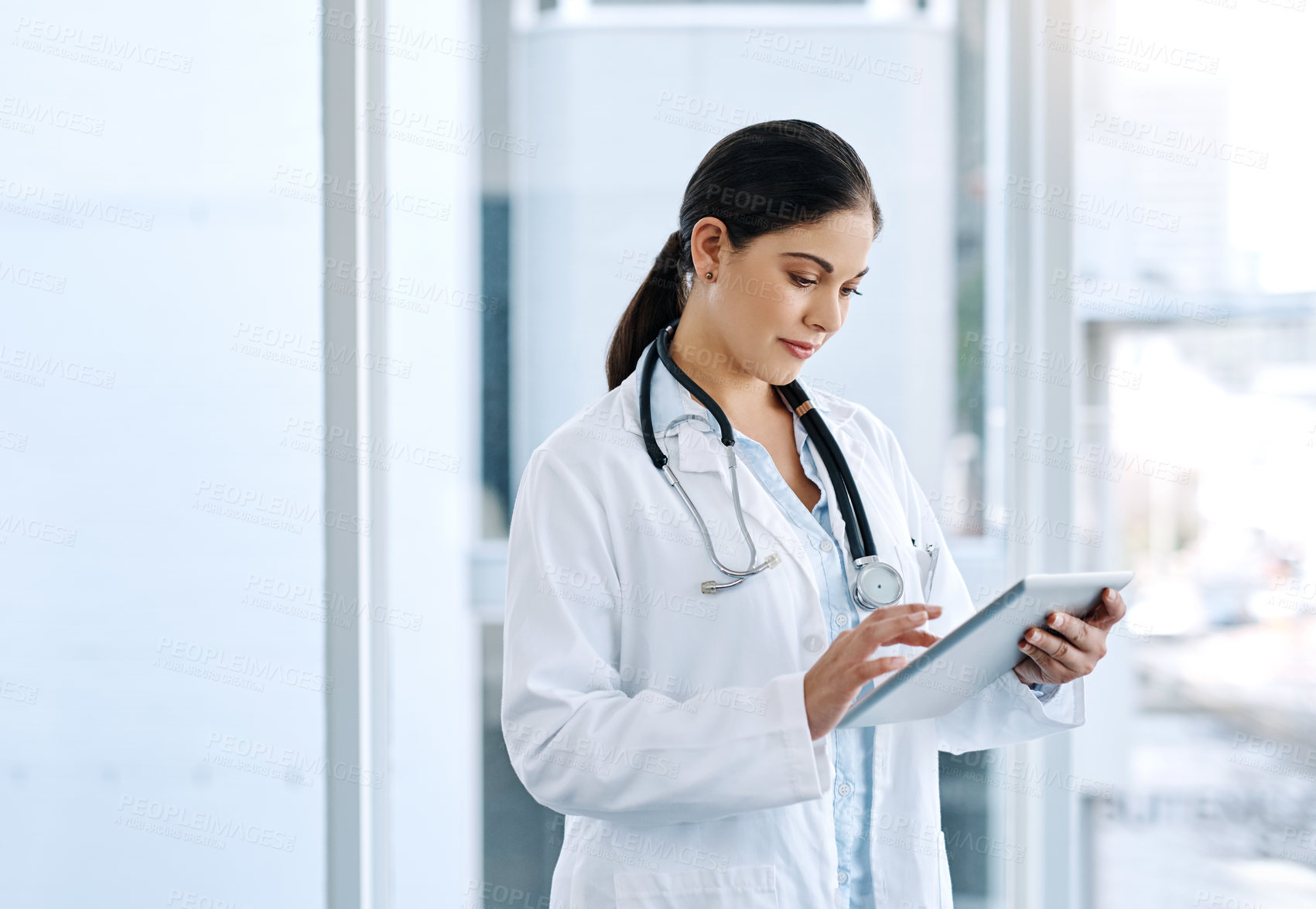 Buy stock photo Shot of a young female doctor using a digital tablet in a hospital