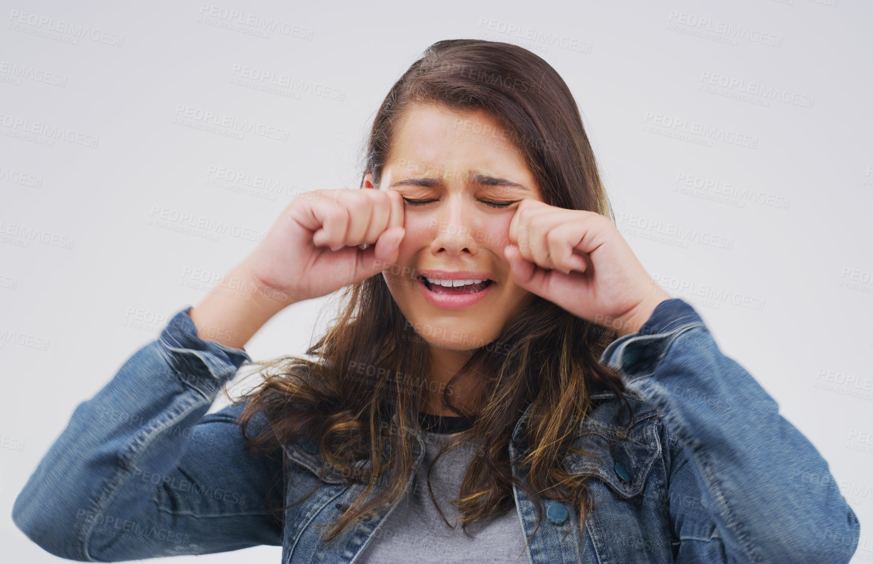 Buy stock photo Studio shot of a young woman crying while standing against a gray background