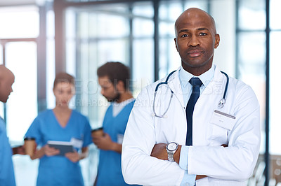 Buy stock photo Portrait of a mature doctor standing in a hospital with his colleagues in the background