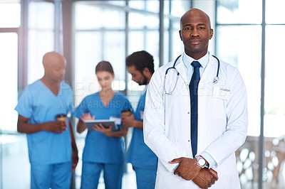 Buy stock photo Portrait of a mature doctor standing in a hospital with his colleagues in the background