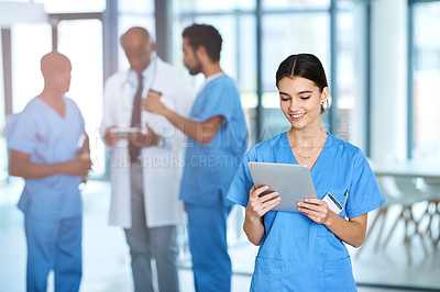 Buy stock photo Shot of a young medical practitioner using a digital tablet in a hospital with her colleagues in the background