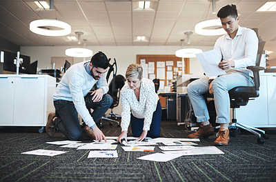 Buy stock photo Full length shot of three young businesspeople working on paperwork together on the floor in the office