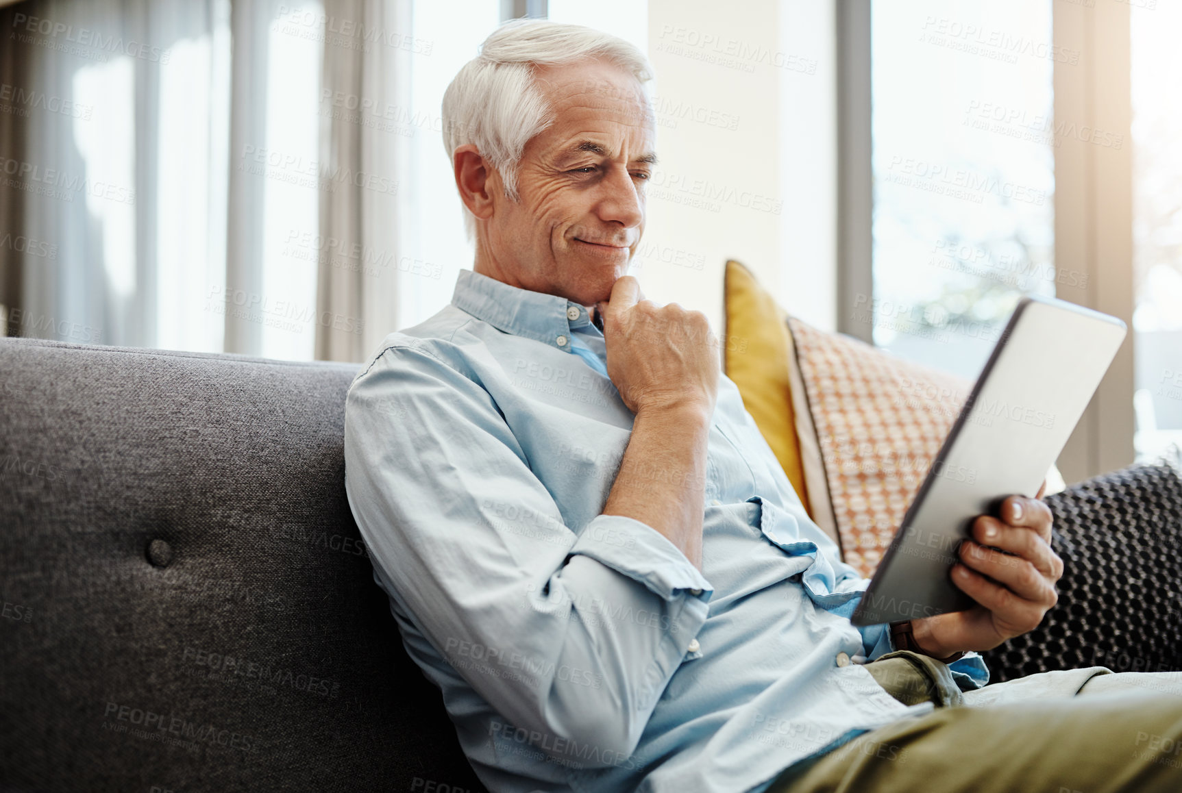 Buy stock photo Shot of a senior man relaxing and using a digital tablet on the sofa at home