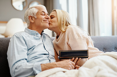 Buy stock photo Shot of mature man giving his wife a gift on the sofa at home