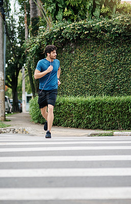 Buy stock photo Shot of a sporty young man running across a road as exercise outside during the day