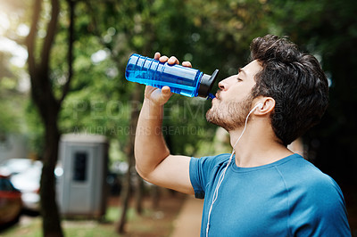 Buy stock photo Shot of a sporty young man drinking water out of a bottle after having a jog outside during the day