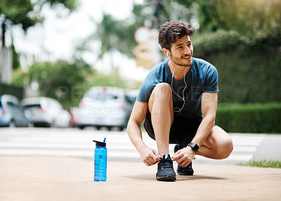 Buy stock photo Shot of a sporty young man tying his shoes before going for a jog outside during the day