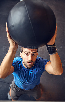 Buy stock photo High angle shot of a handsome young man working out with a medicine ball in the gym