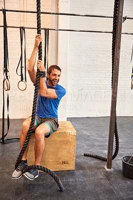Buy stock photo Full length shot of a handsome young man rope climbing while working out in the gym