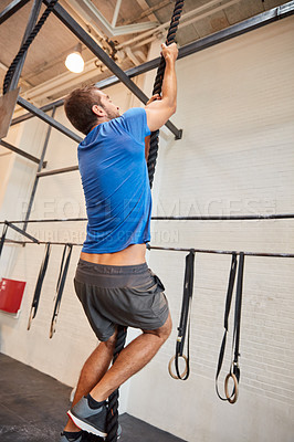 Buy stock photo Full length shot of a handsome young man rope climbing while working out in the gym