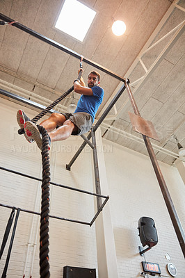 Buy stock photo Low angle shot of a handsome young man rope climbing while working out in the gym