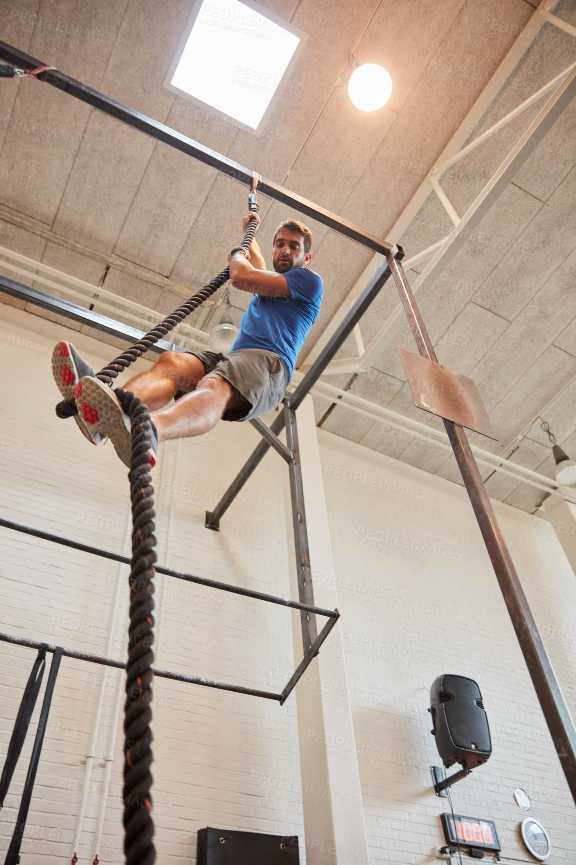 Buy stock photo Low angle shot of a handsome young man rope climbing while working out in the gym
