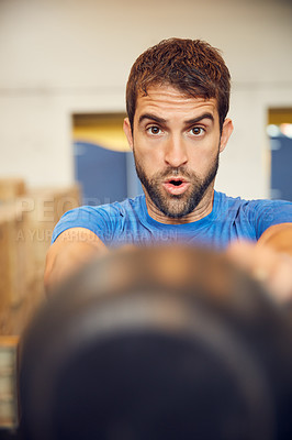 Buy stock photo Cropped portrait of a handsome young man working out with a kettle bell in the gym