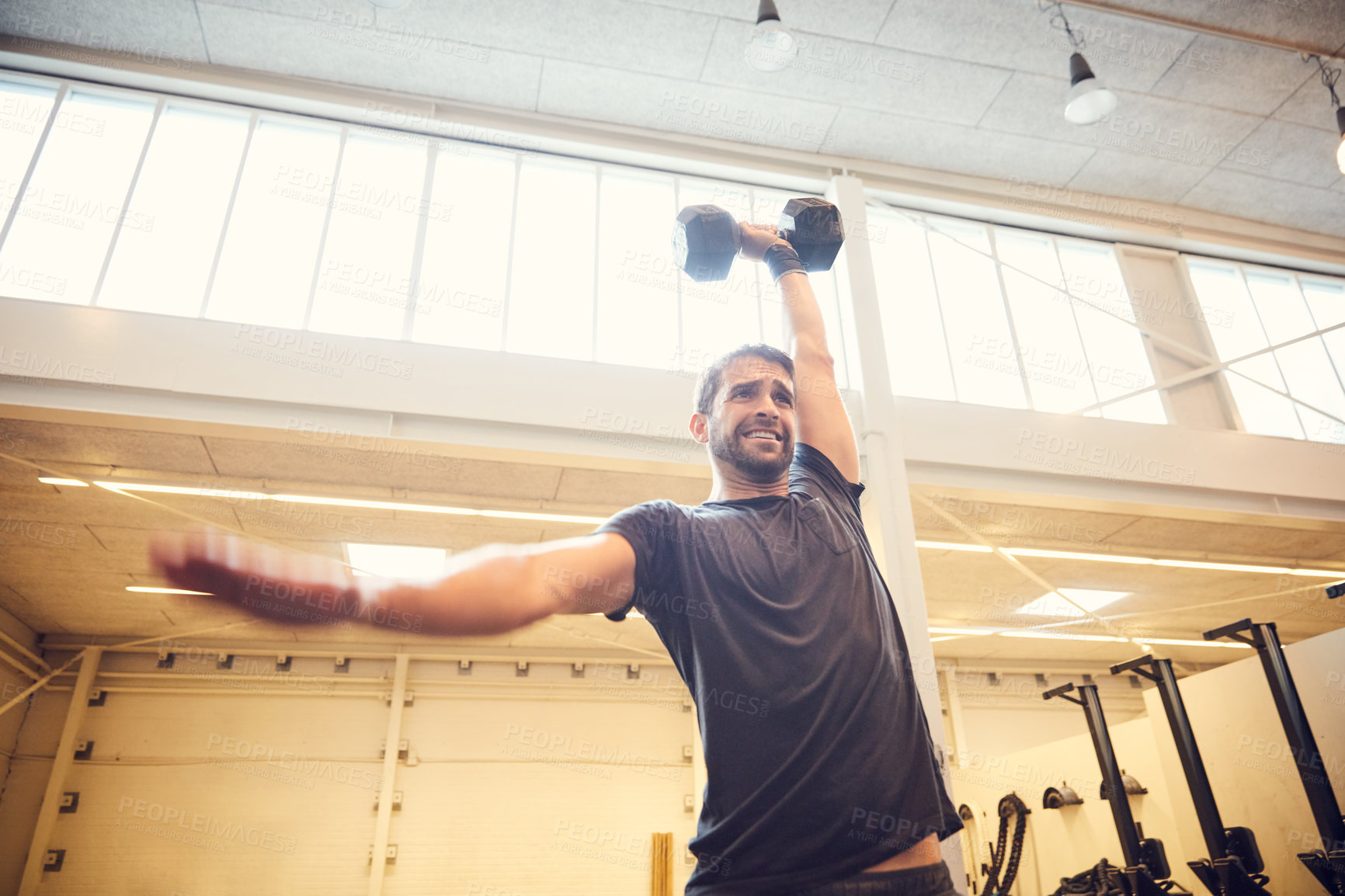 Buy stock photo Low angle shot of a handsome young man working out with a dumbbell in the gym