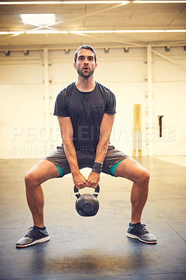 Buy stock photo Full length shot of a handsome young man working out with a kettle bell in the gym