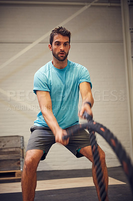 Buy stock photo Cropped shot of a handsome young man working out with battle ropes in the gym