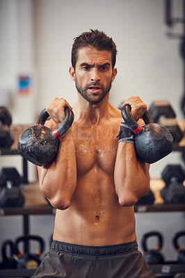 Buy stock photo Cropped shot of a handsome young man working out with kettle bells in the gym