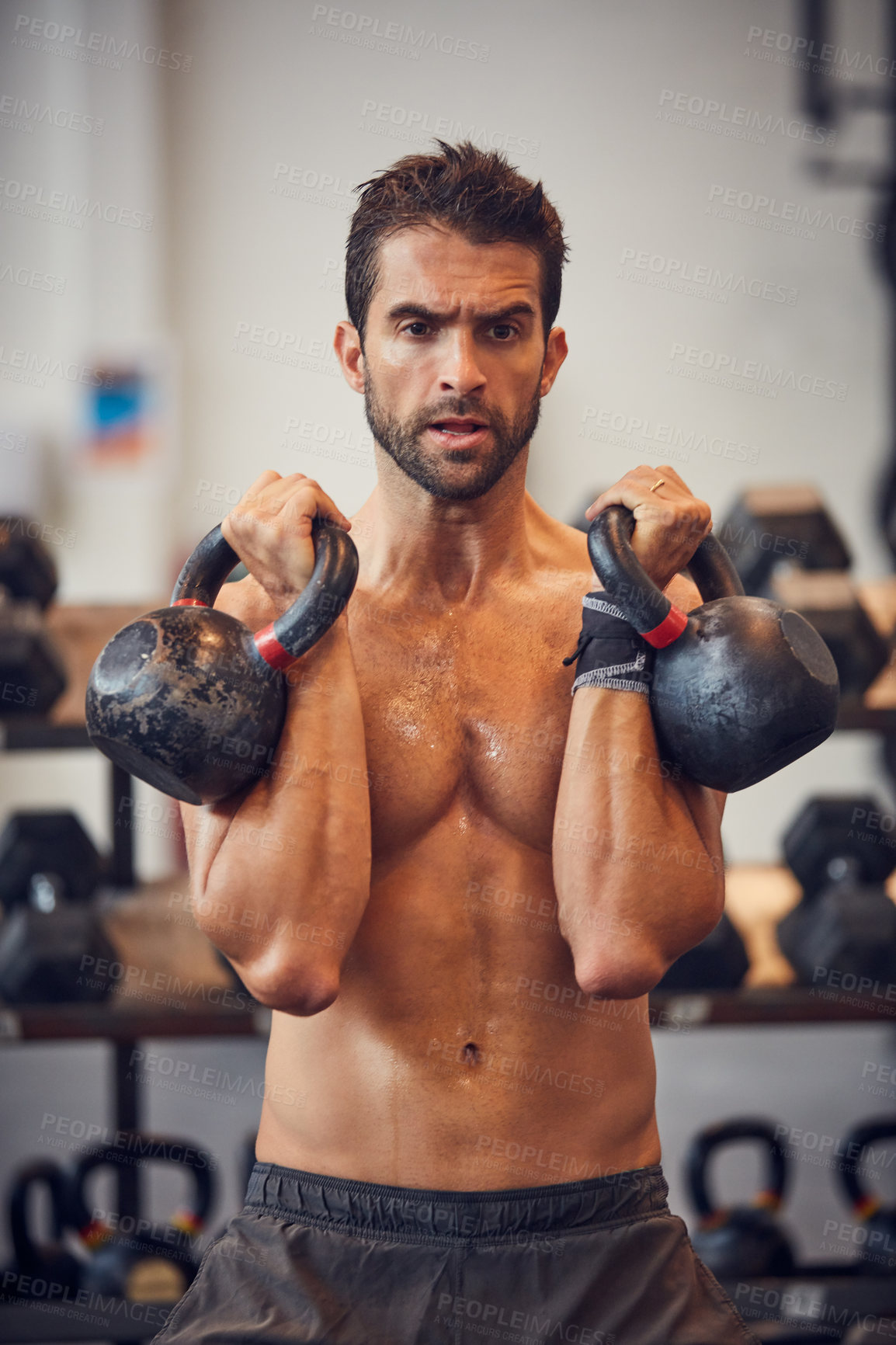 Buy stock photo Cropped shot of a handsome young man working out with kettle bells in the gym