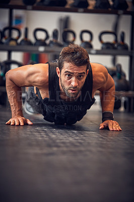 Buy stock photo Full length shot of a handsome young man doing pushups while working out in the gym