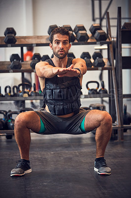 Buy stock photo Cropped shot of a handsome young man doing squats while working out in the gym
