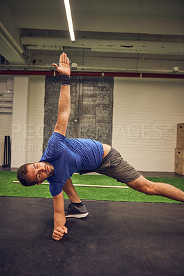Buy stock photo Cropped shot of a handsome young man stretching while working out in the gym