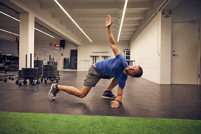 Buy stock photo Full length shot of a handsome young man stretching while working out in the gym