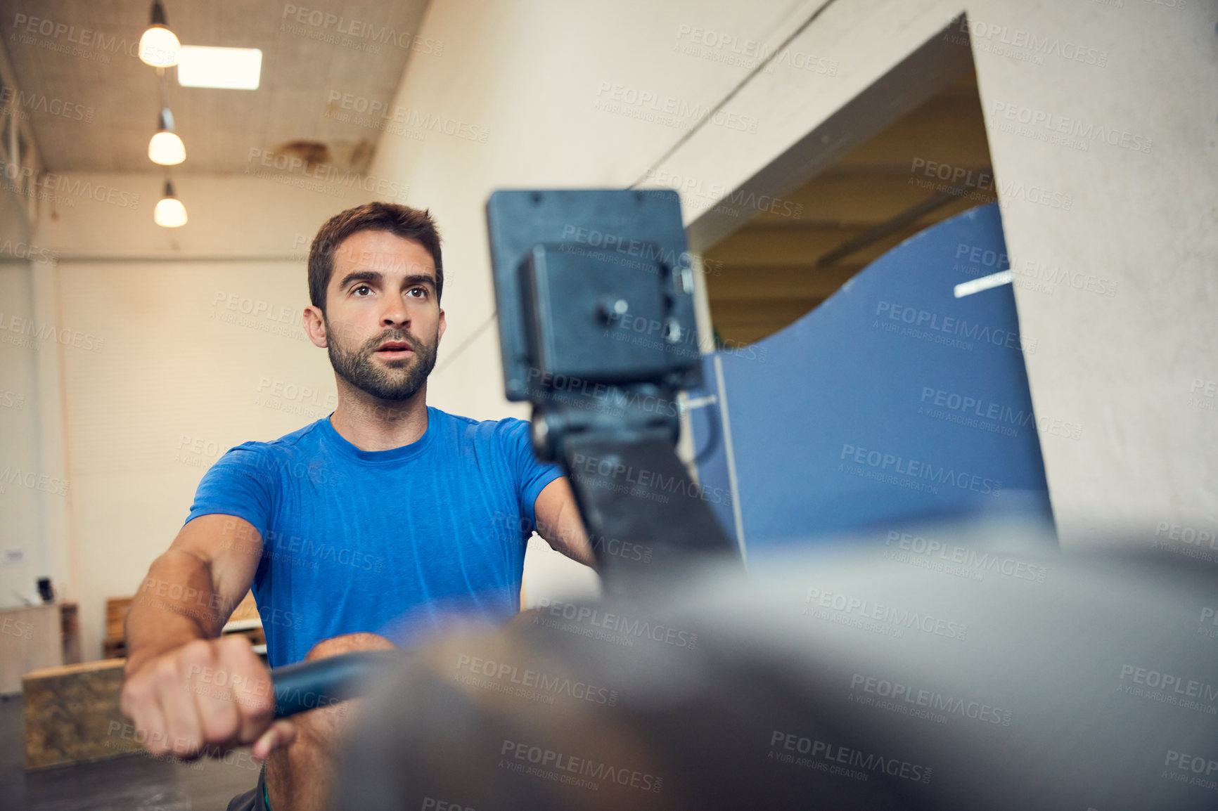 Buy stock photo Low angle shot of a handsome young man working out on a rowing machine in the gym