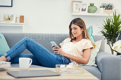 Buy stock photo Shot of an attractive woman using her cellphone while relaxing at home