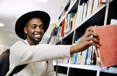 Buy stock photo Shot of a happy young man removing a book from a shelf in a college library