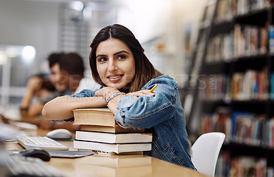 Buy stock photo Shot of a young woman resting on a pile of books in a college library and looking thoughtful
