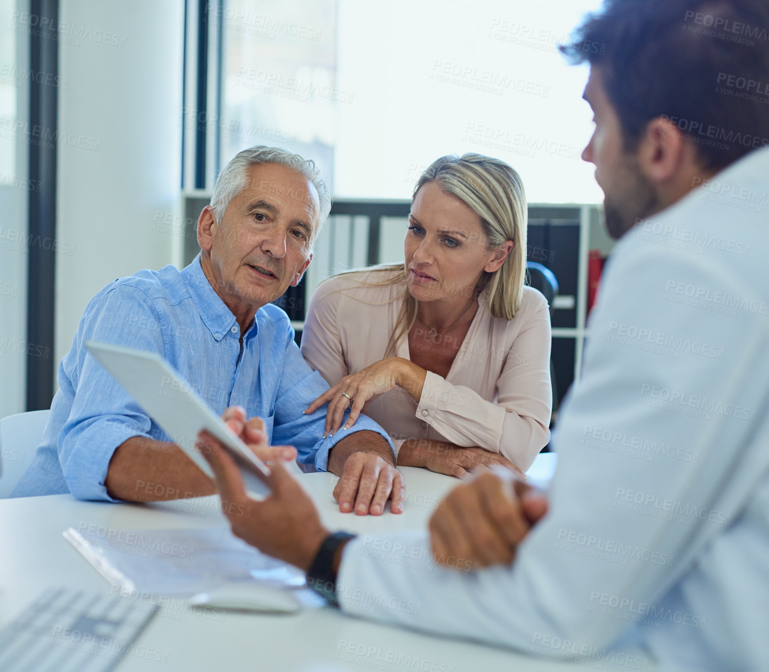 Buy stock photo Shot of a doctor discussing findings on his digital tablet with a senior patient and his daughter at the clinic