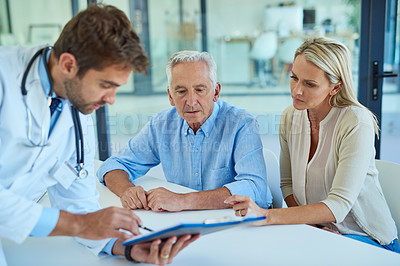 Buy stock photo Shot of a doctor discussing some paperwork with a senior patient and his daughter in a clinic