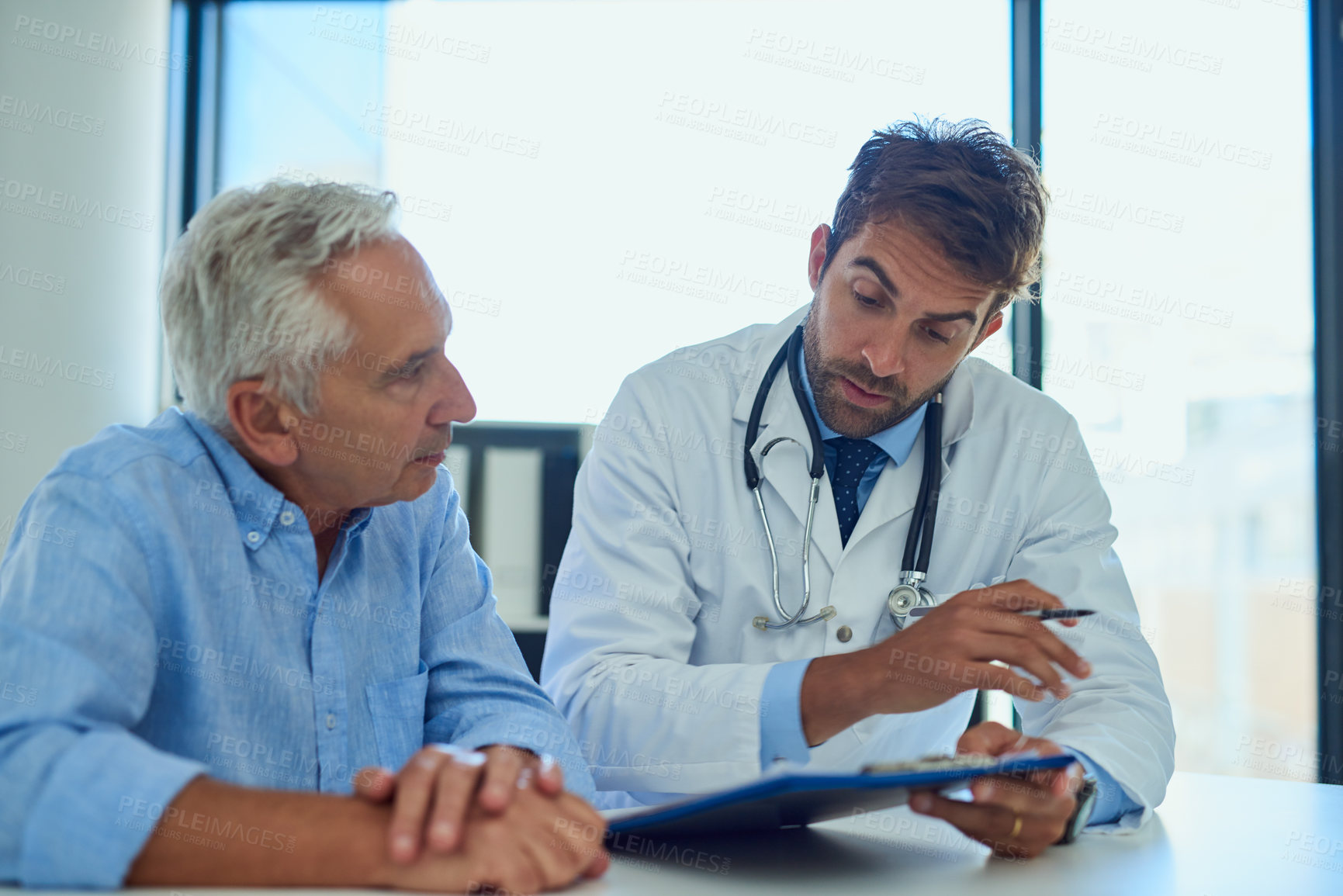 Buy stock photo Shot of a handsome doctor going over some paperwork with a male senior patient in a clinic